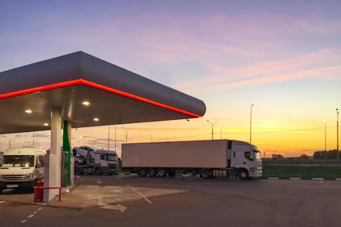 Stacja benzynowa, na której stoi ciężarówka, na tle wschodzącego słońca.